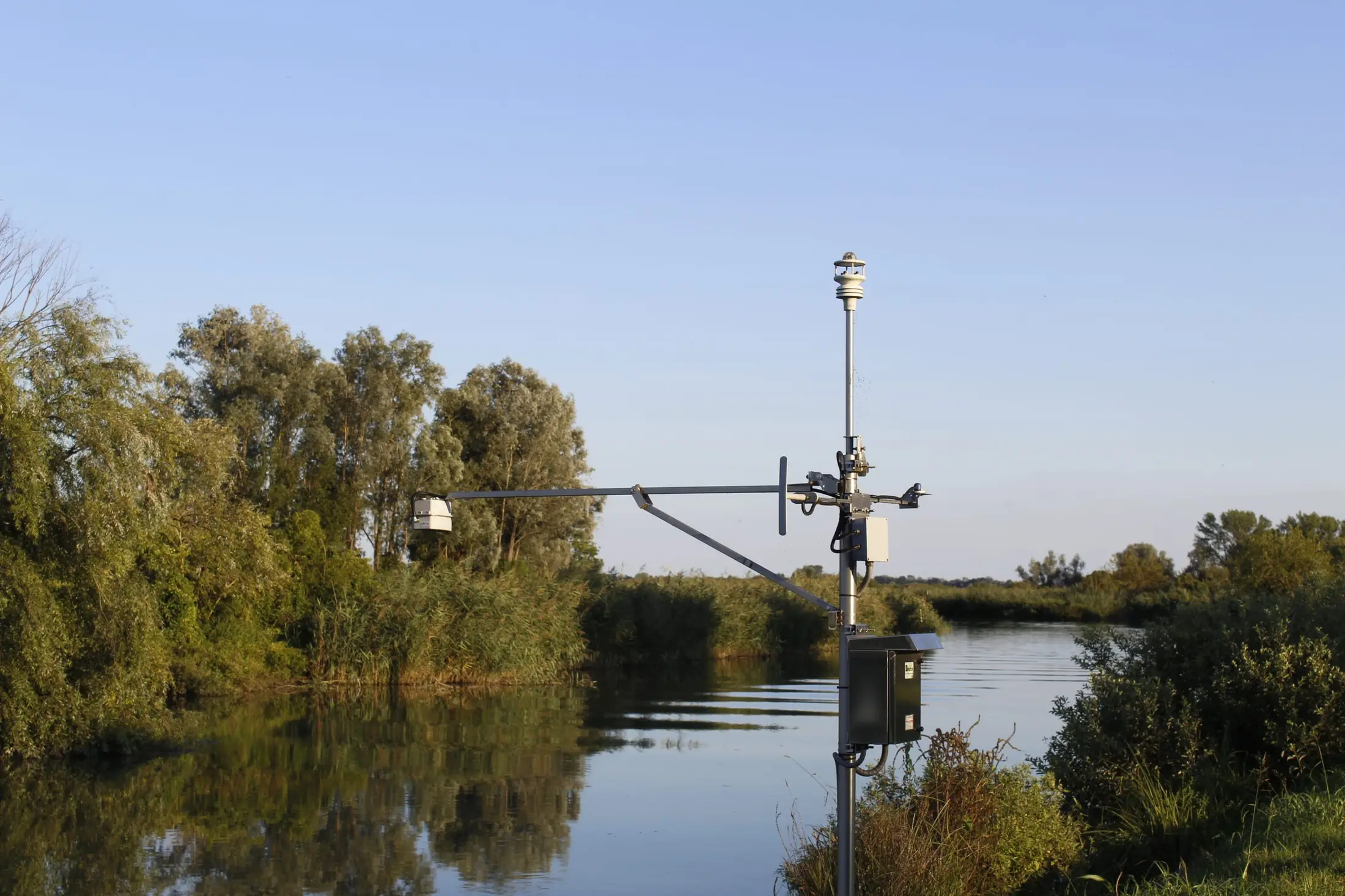 La stazione di rilevamento sulla riva del Mincio, fra i salici, con il fiume calmo che riflette il canneto