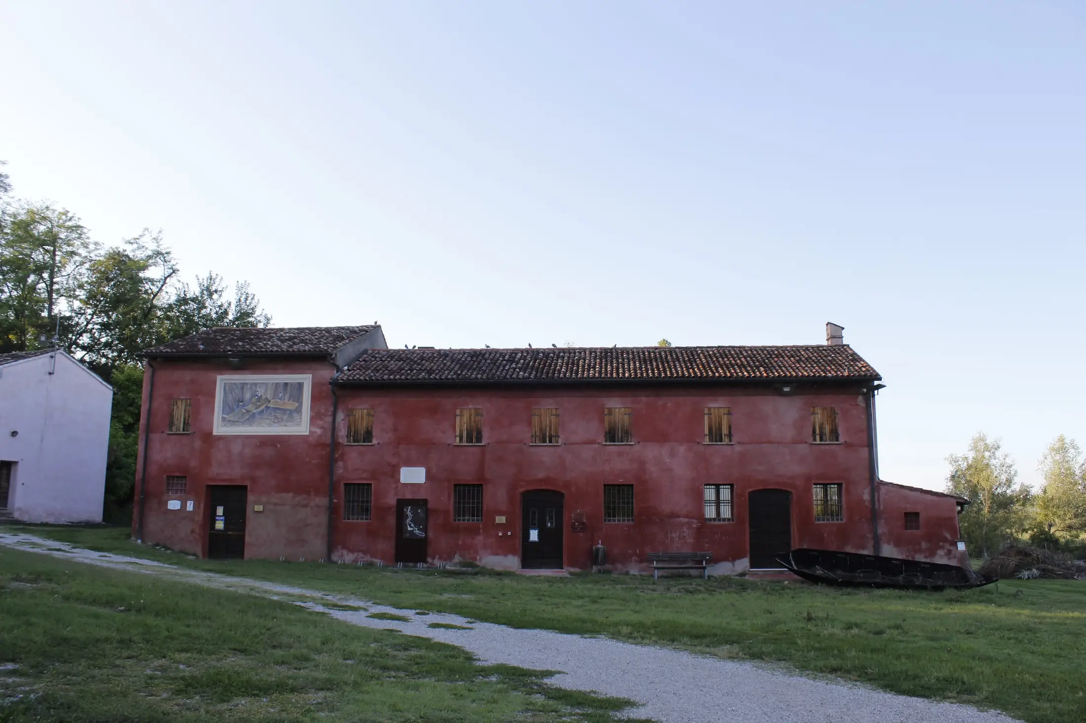 Il Museo Etnografico dei Mestieri del Fiume: la lunga facciata rossa col mosaico e una barca in legno appoggiata di fianco